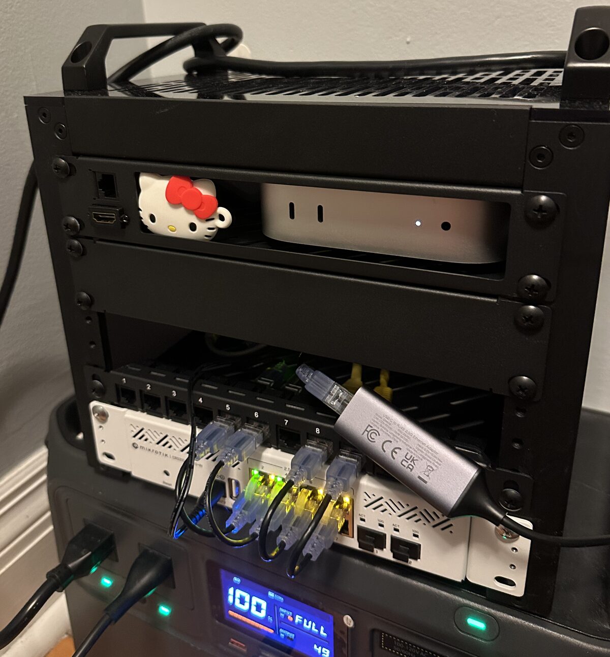 10-inch mini rack: a Mac mini node above a patch panel and MikroTik switch, sitting on a battery power station